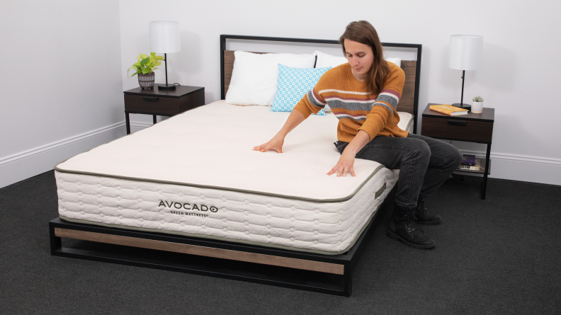 A person sitting on and pressing their hands into the Avocado Green Mattress.