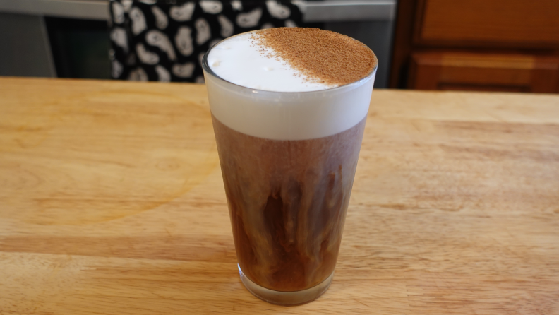 A cold brew pumpkin spice latte with cold foam on a wooden counter.