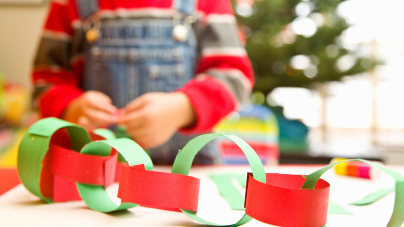Child in front of Christmas tree creating a paper chain garland with red and green paper