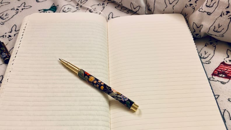 a journal sits open on a bed near a pillow with an uncapped pen