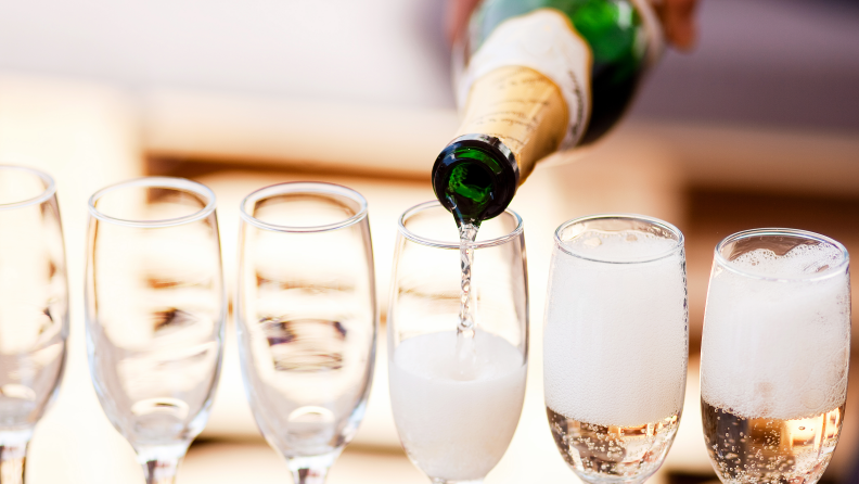 A row of champagne flutes being filled by a bottle of campagne.