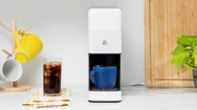 Beautiful coffee maker on a white kitchen counter, with two brewed cups of coffee beside it.