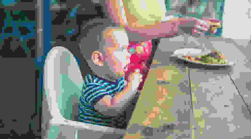 A toddler sits on a booster seat at the dinner table.