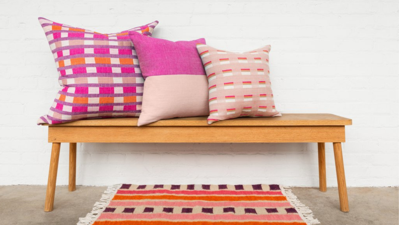 Bright pink pillows on wooden bench next to bright pink and orange rug