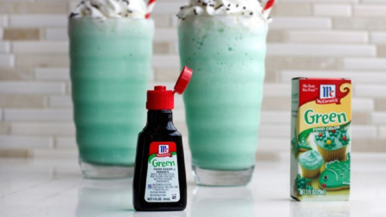 An image of a bottle of McCormick green dye next to its box, in front of two pale green shakes.