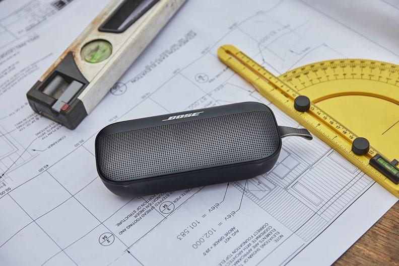 A Bose portable speaker sitting on some blueprints next to a protractor and a bubble level.