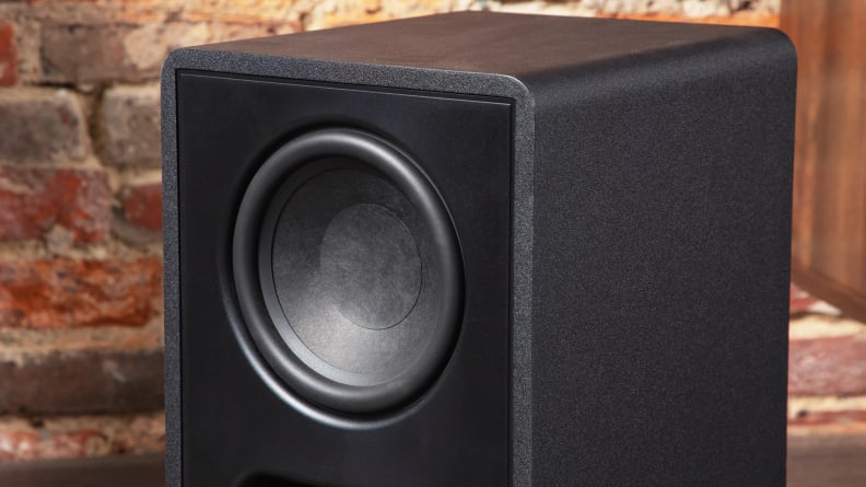 Close up shot of black wireless subwoofer sitting in front of brick wall.