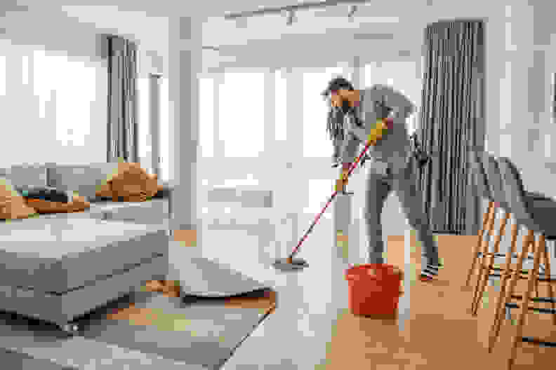 Young man cleaning his apartment with a mop.