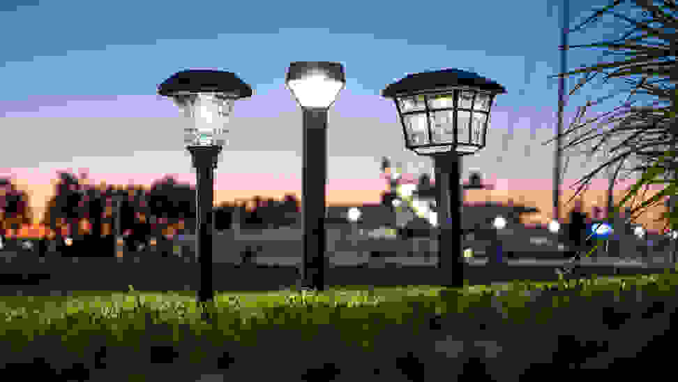 A row of outdoor solar path lights in a park, set against a sunset