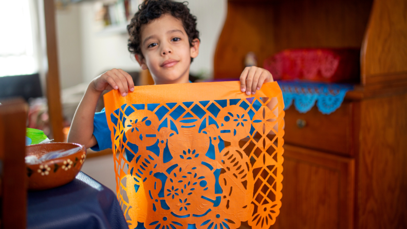 Small child holding up an orange Papel Picado square.