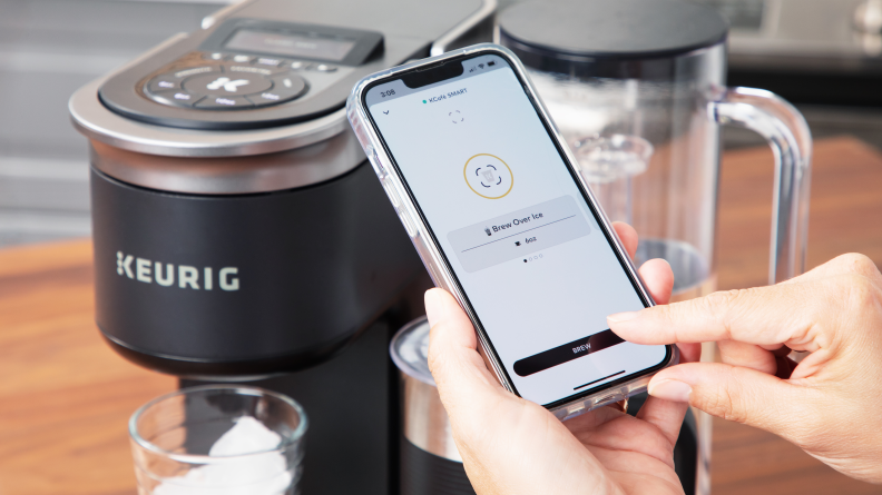 A close up of a person using the app on a smartphone to control the Keurig K-Cafe Smart coffee machine.