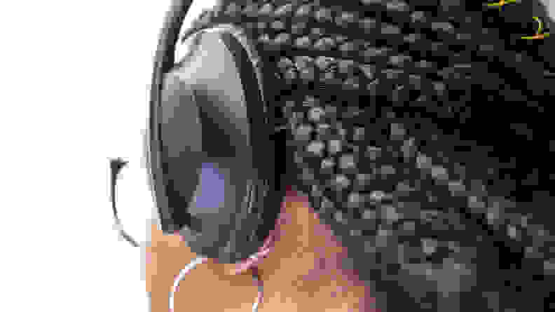 The back of a woman's head, wearing the Bose 700 wireless active noise-cancelling headphones. We can see a few small buttons along the  outside edge of the ear cups.