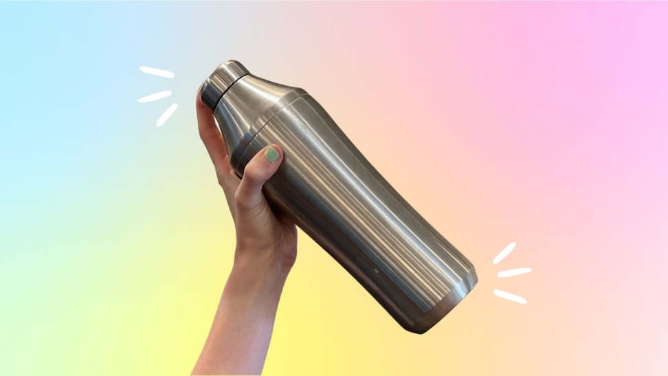 A hand holds a stainless steel cocktail shaker against a rainbow gradient background.