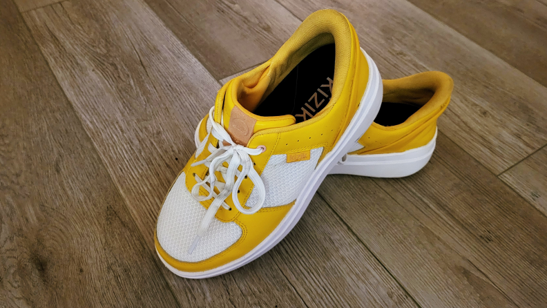 Side view of bright yellow and white Kizik Brisbane sneakers on woodgrain flooring