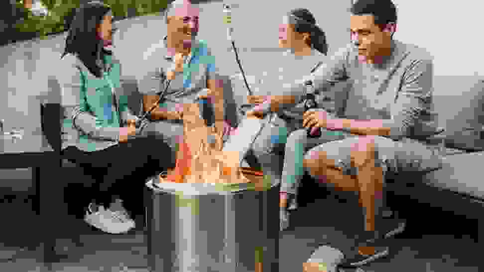 Group of people sitting around the Solo Stove Bonfire fire pit roasting marshmellows