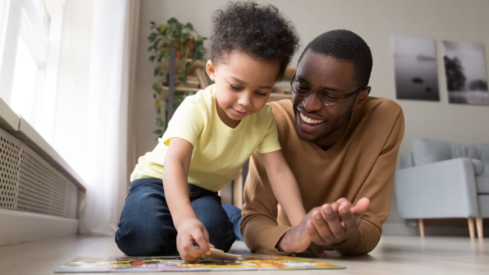 A parent and child put together a puzzle on a floor together.