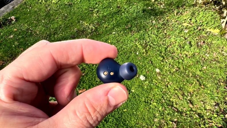 The interior of a navy earbud sits in a hand in front of a grassy backdrop.