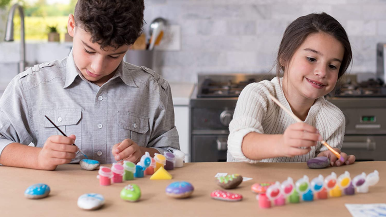 Two children painting rocks at a table