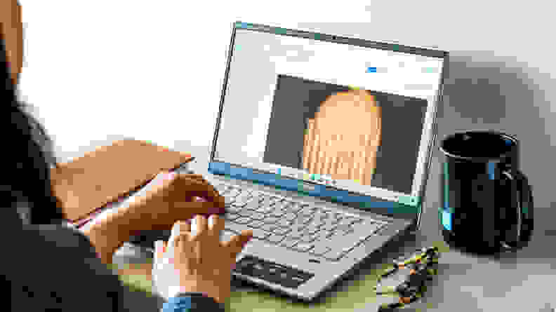 A person holds their fingers over a laptop's keyboard and trackpad while working on a project.