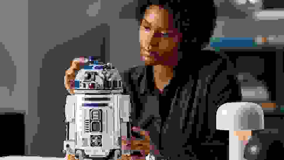 A person finishes assembling a large LEGO Star Wars R2-D2 kit.