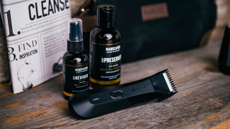 A beard trimmer laying on a table next to bottles of grooming products.