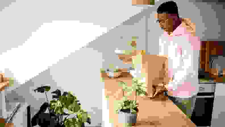 A Black man unloading groceries and wine from a paper bag in his kitchen