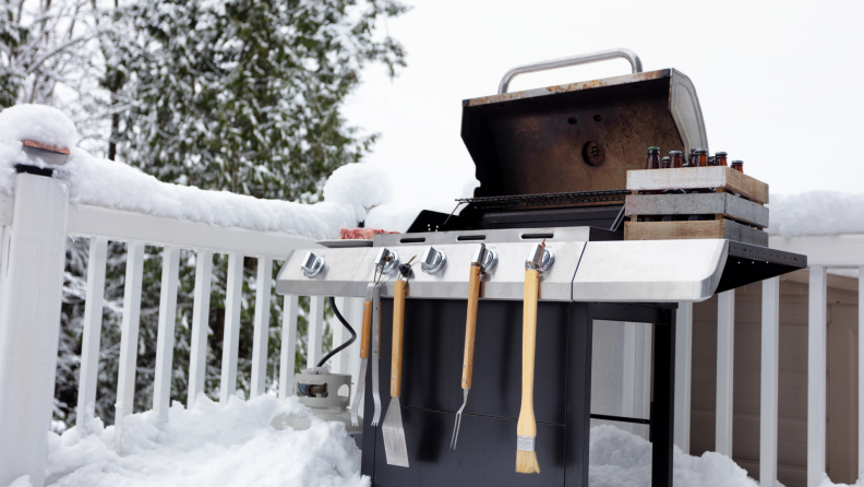 Open grill with grill accessories attached on snowy outdoor deck