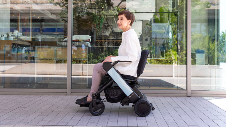 A person uses a wheelchair to travel on the sidewalk.