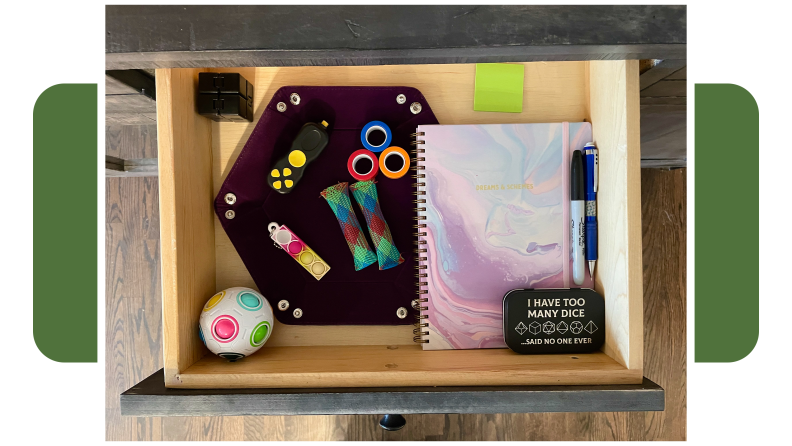Small drawer filled with Dungeons and Dragons game items including dice, a notebook, writing utensils, and several fidget toys.