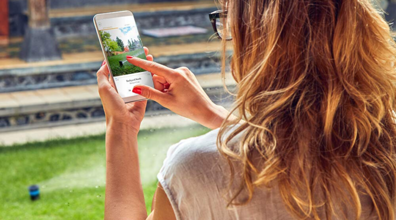 A woman users the Rachio app outside to access her smart sprinkler controller.