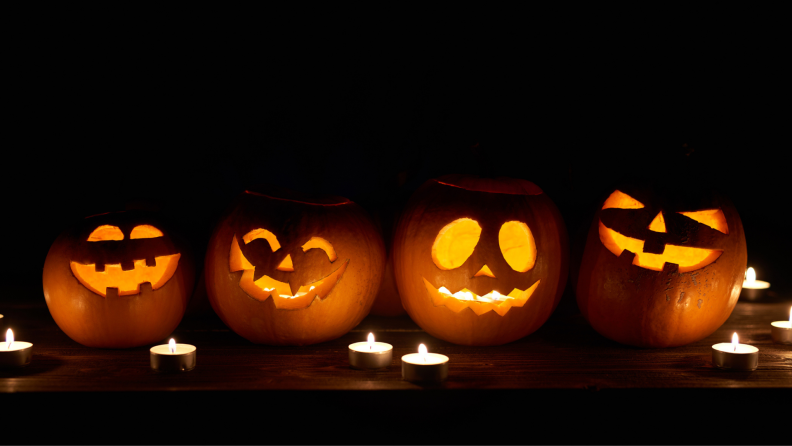 Four jack-o-lanterns lit and surrounded by tealight candles