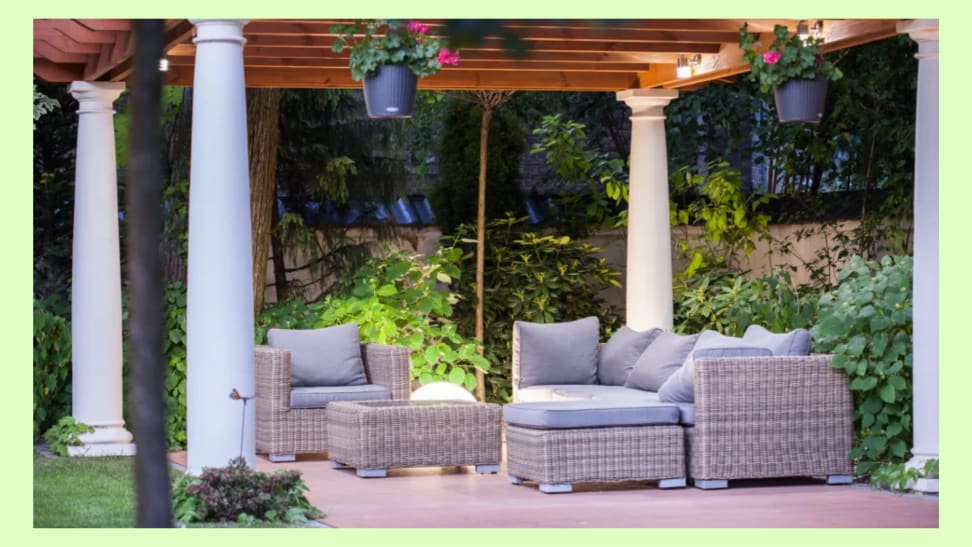A patio space with a matching outdoor sofa and chair surrounded by green shrubbery.