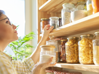 A woman holds a jar of sugar inside her organized pantry full of canned items.