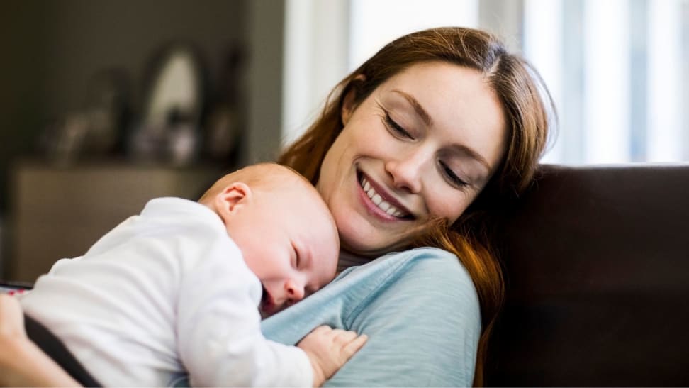 Smiling redhead mother is sitting with her sleeping newborn child