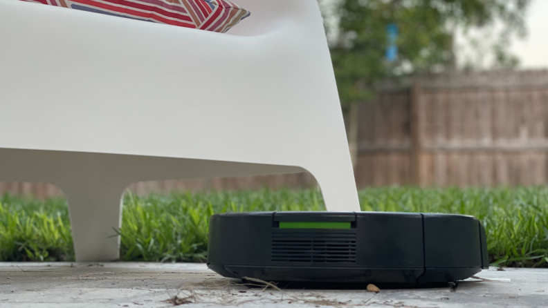 An iRobot vacuum on a patio with a chair in the background.