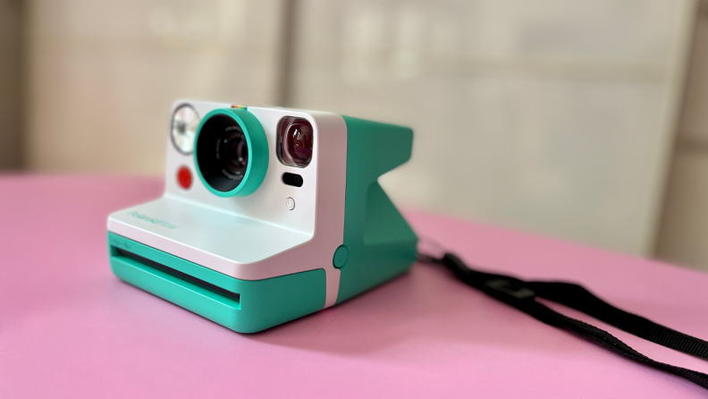 Teal and white polaroid film camera on pink tabletop surface.