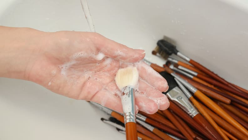 A person washing makeup brushes.