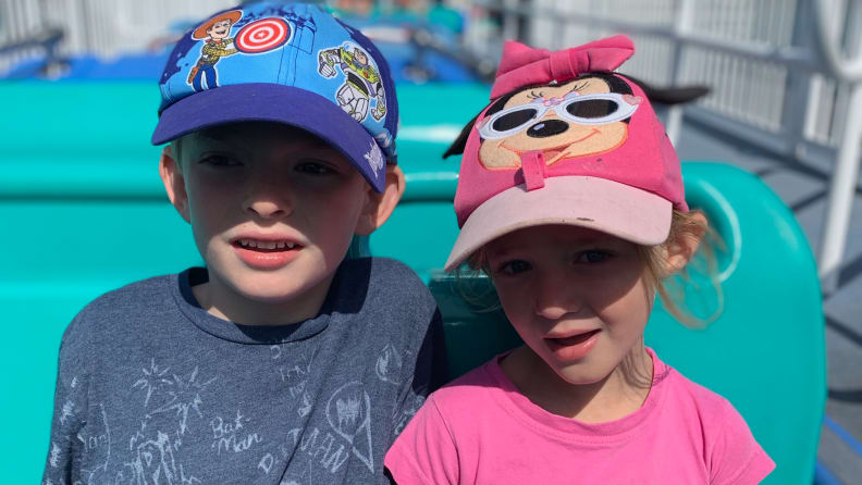 A young boy wearing a Toy Story baseball cap sitting next to a young girl wearing a pink mini mouse hat