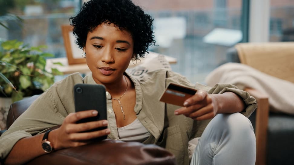 A woman sits in a chair holding her phone and credit card