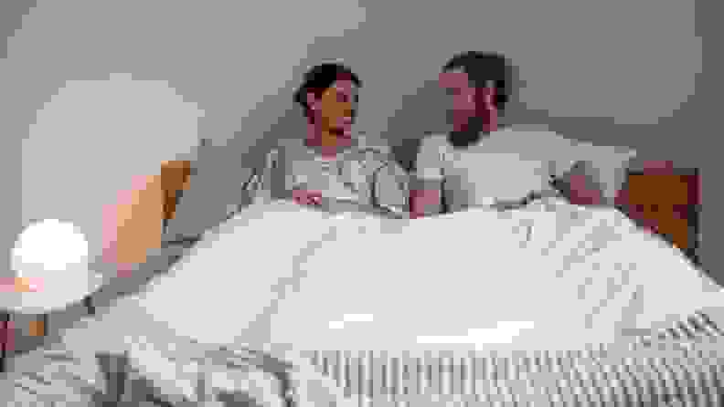 a man and woman sit in bed talking