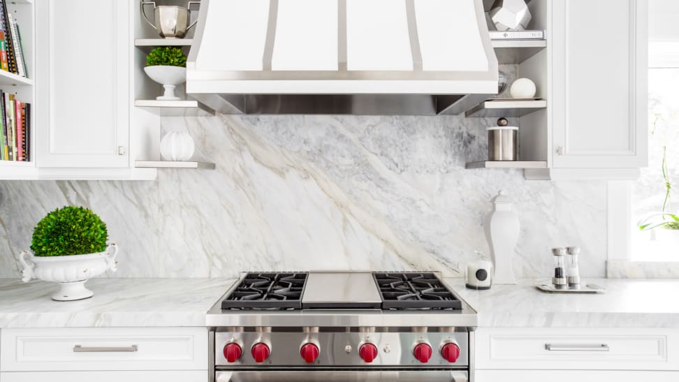 A modern kitchen with a white range hood over a stainless steel stove and oven.