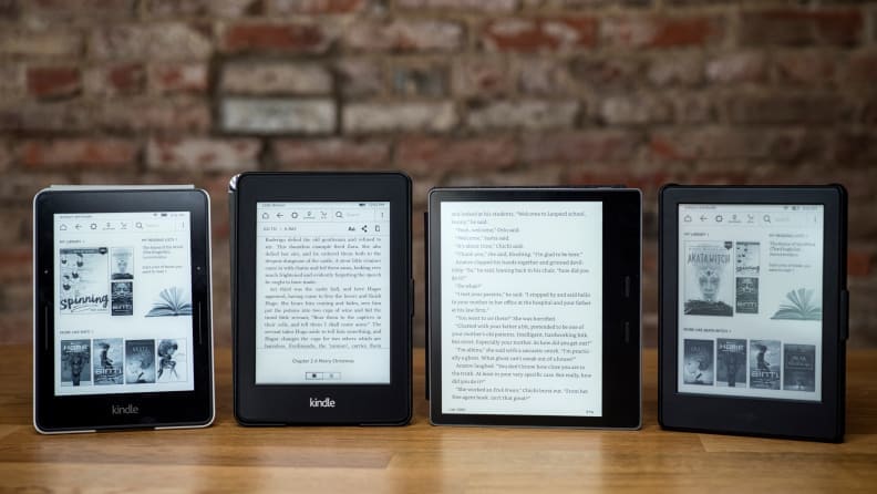 Four Kindles, including the entry-level model, the Paperwhite, and the Oasis, lined up against an exposed brick wall.