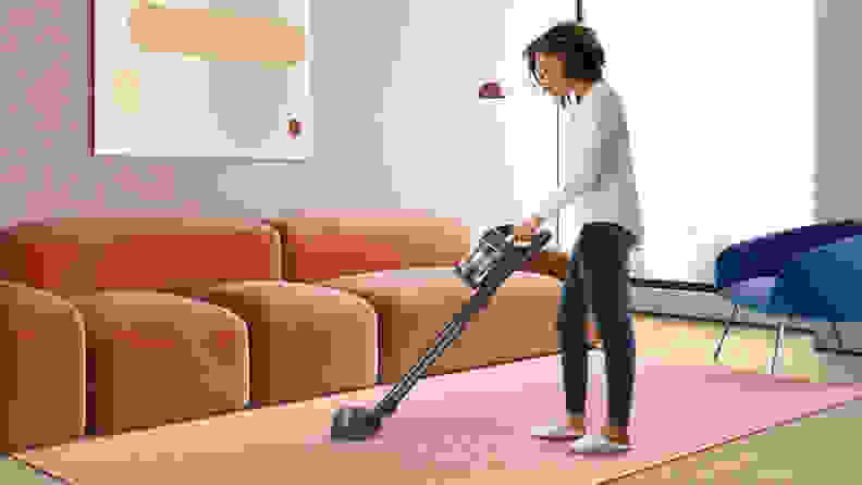 Woman cleaning a pink carpet with a cordless stick vacuum cleaner.