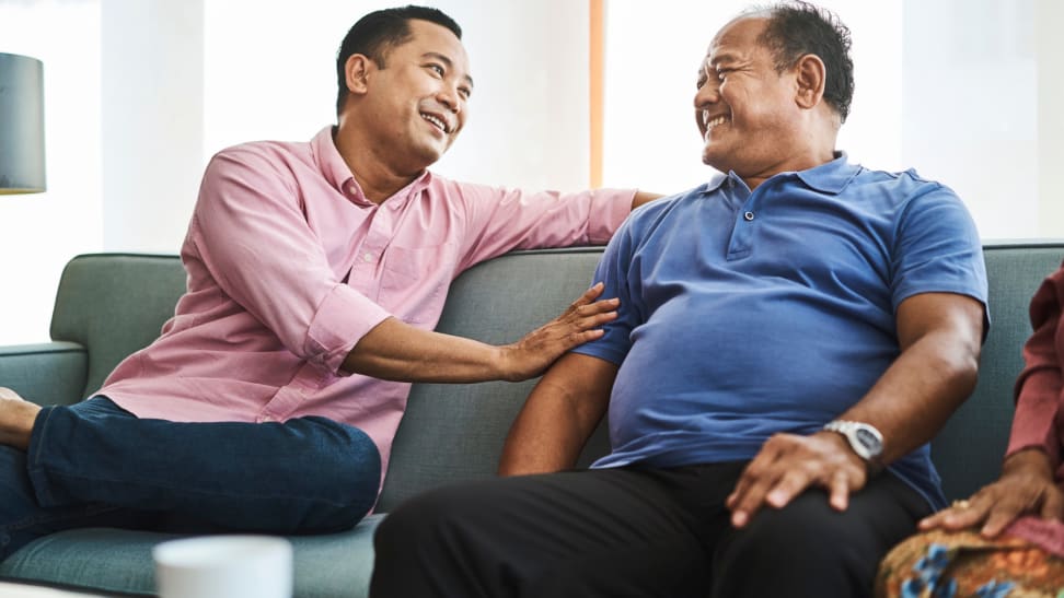 Two older people sitting on couch together while smiling and enjoying a conversation.