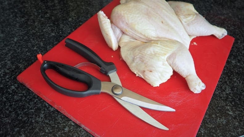 A raw chicken and a pair of poultry shears on top of a red plastic cutting board.