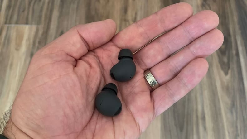 A man holds a pair of the Samsung Galaxy Buds 2 Pro earbuds in his hand above a wooden floor.