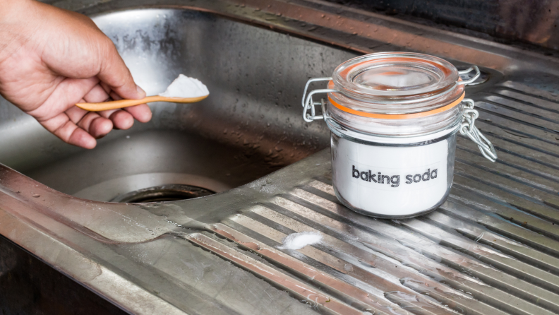 Person sprinkling baking soda into drain in sink.