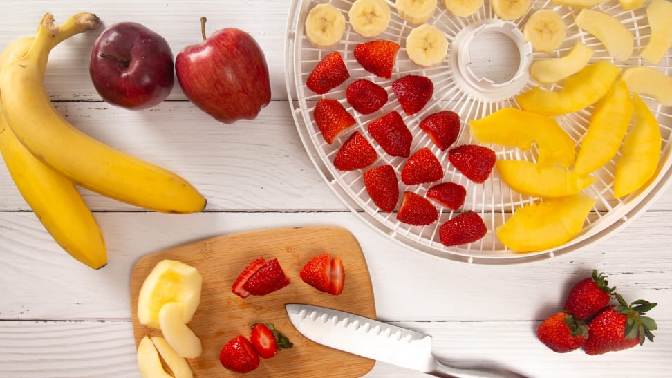 A photo of whole apples and bananas arranged next to a platter of sliced bananas, apples, peaches, and strawberries.