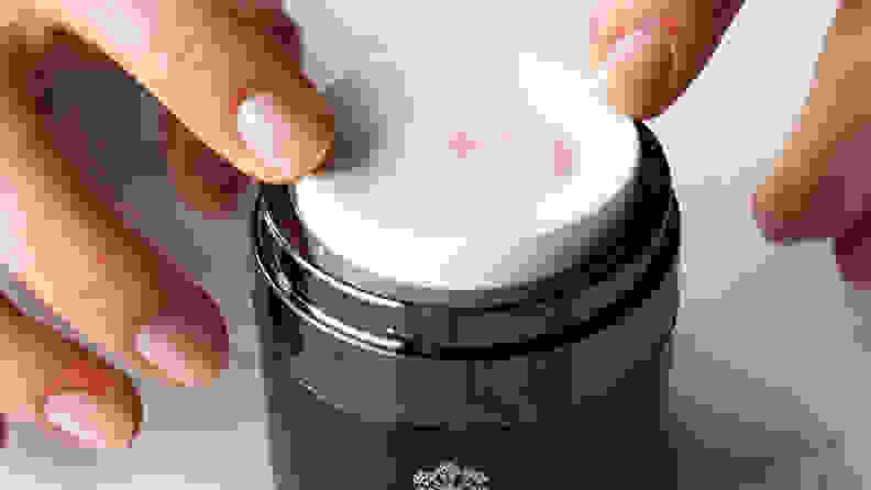 A black jar with a white lid and a pink liquid coming through a whole in the white lid.