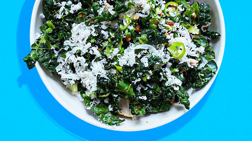 A kale salad topped with feta cheese, served in a white bowl and placed on a blue background.